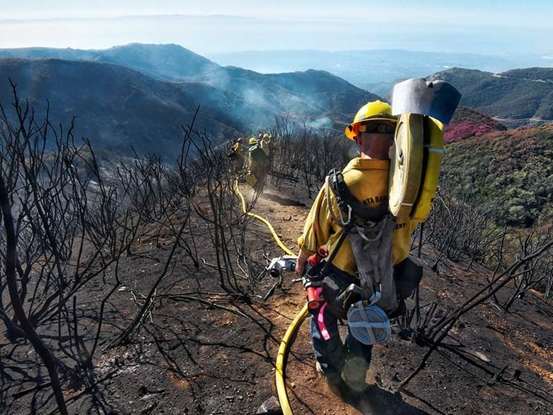 In this photo provided by the Santa Barbara County Fire Department, Santa Barbara County Firefighters haul hose and equipment down steep terrain to root out and extinguish smoldering hot spots in Santa Barbara, Calif., Tuesday, Dec. 19, 2017.